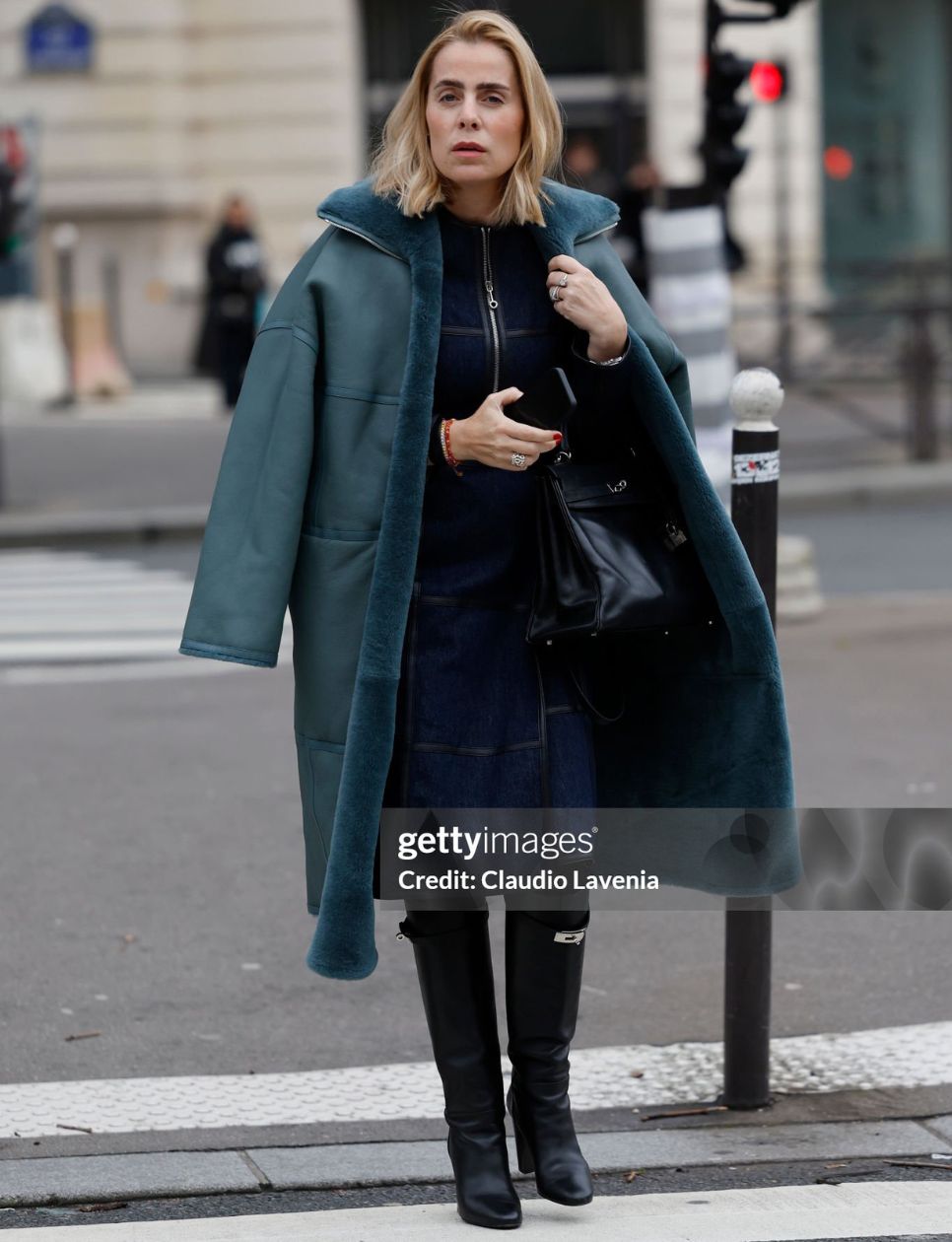 A guest wears blue denim jacket with matching midi skirt, teal coat with fur details, black Hermès boots, black Hermès bag, outside Hermès, during the Menswear Fall Winter 2025/2026 as part of Paris Fashion Week on January 25, 2025 in Paris, France. (Photo by Claudio Lavenia/Getty Images)