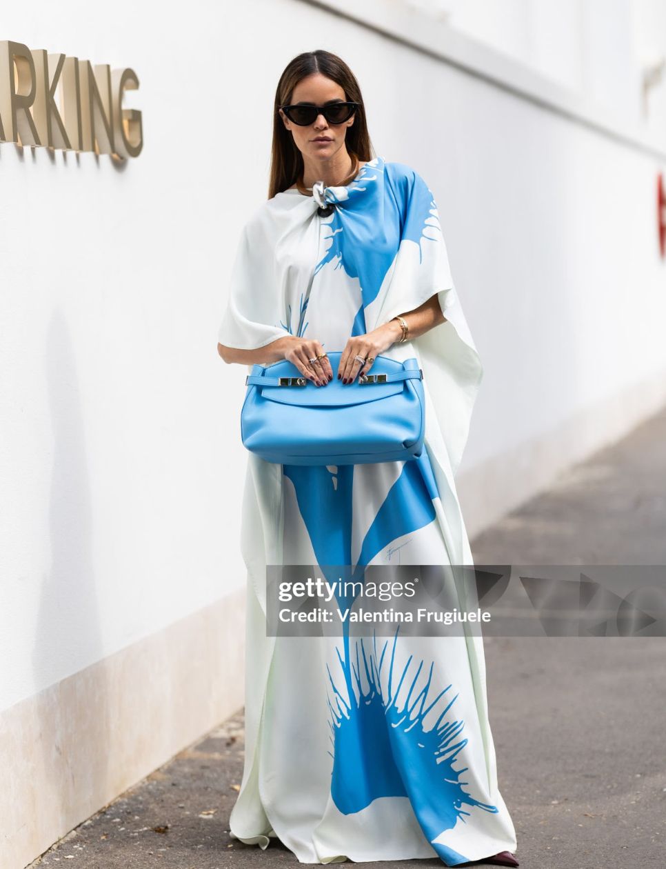 A guest wears black sunglasses, a light blue leather Ferragamo bag and a white and light blue printed kaftan dress outside the Ferragamo show during the Milan Fashion Week Menswear Spring/Summer 2025 on September 21, 2024 in Milan, Italy. (Photo by Valentina Frugiuele/Getty Images)