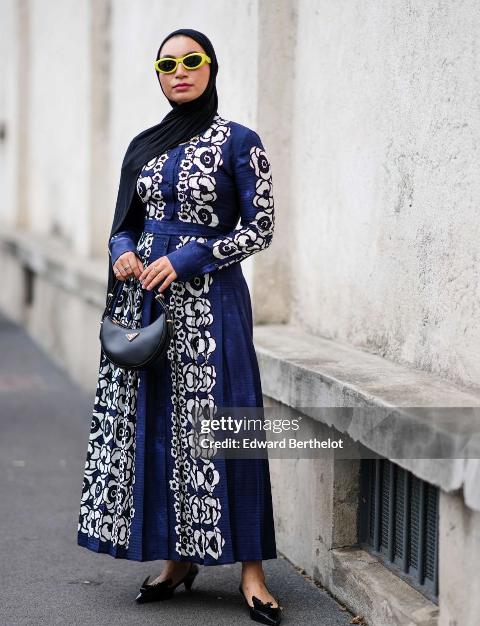 A guest wears a black scarf on the head, yellow sunglasses, a Prada dark blue maxi dress with a white floral pattern, a black Prada bag, black pointy Prada shoes , outside Prada, during the Milan Fashion Week - Womenswear Spring/Summer 2024 on September 21, 2023 in Milan, Italy. (Photo by Edward Berthelot/Getty Images)