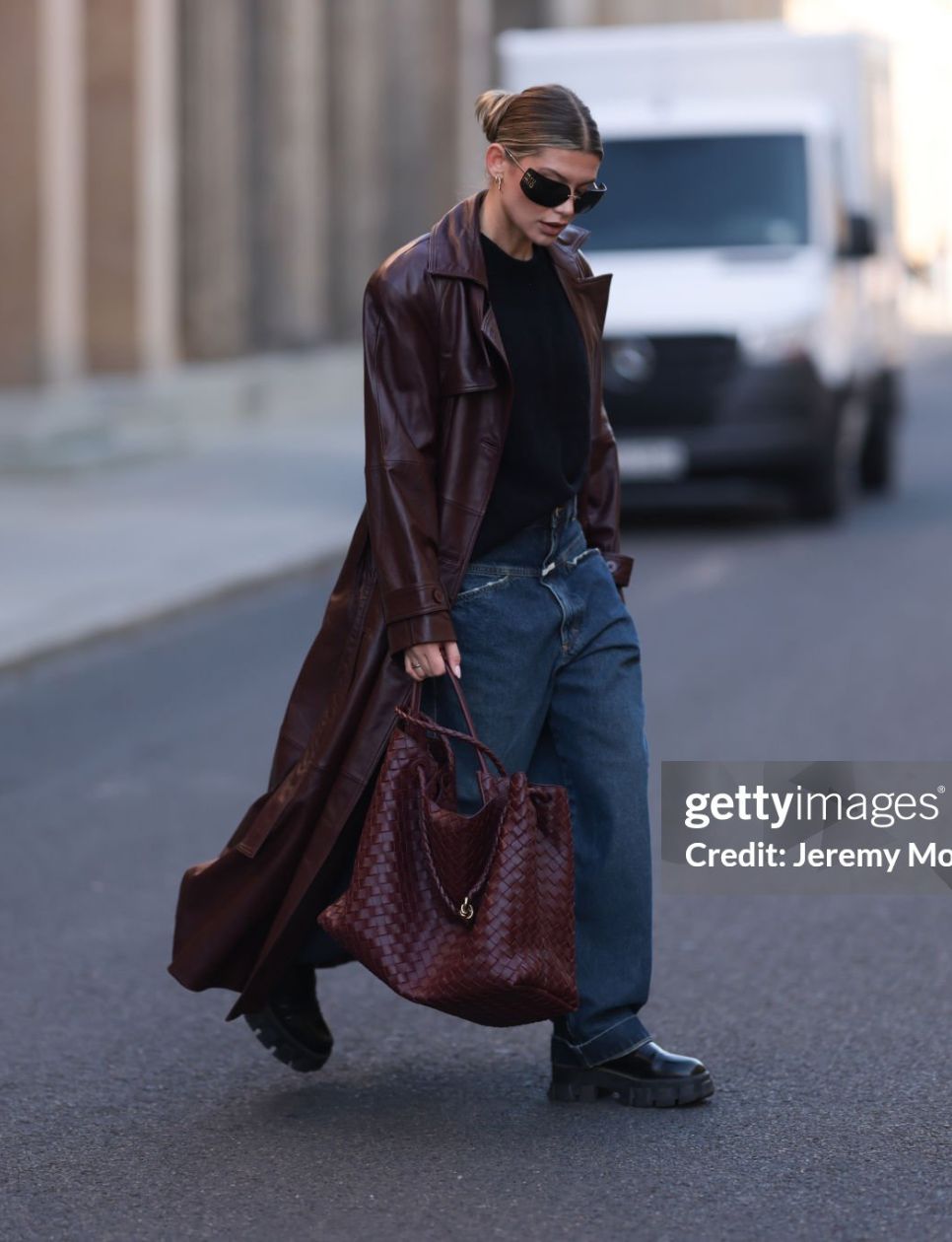 Sophia Geiss is seen wearing rimless oversized sunglasses with brown curved lenses with logo-embellishment, slim gold metal temples paired with the matching gold metal nose bridge from Miu Miu; two different-sized gold hoop earrings; a silver nose ring; an ankle-length burgundy leather coat with large notch lapels, belted cuffs, and a tie belt from Ducie London; a black knit pullover with round neckline underneath; wide-legged jeans from Closed; a large “Andiamo“ bag in burgundy woven leather from Bottega Veneta; a silver ring; and black leather boots with chunky sole from Prada on October 23, 2024 in Berlin, Germany. (Photo by Jeremy Moeller/Getty Images)