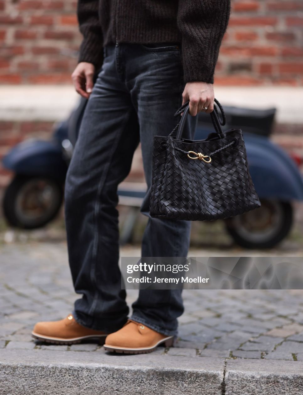 Paul Maximilan is seen wearing a brown chunky rib-knitted cardigan from Weekday, the rectangular black woven leather “Andiamo“ bag with gold knot detail from Bottega Veneta, grey straight-legged jeans, a silver ring, and brown suede lace-up boots with rubber soles from Timberland on September 23, 2024 in Munich, Germany. (Photo by Jeremy Moeller/Getty Images)