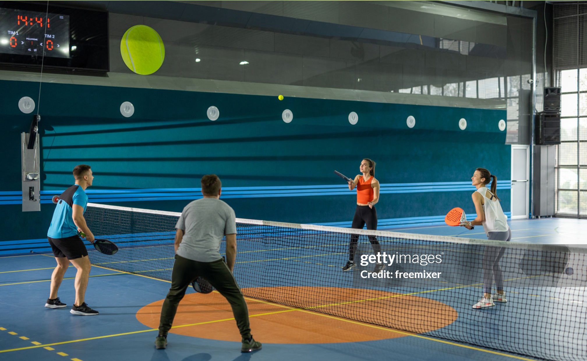 Wide shot of young friends playing doubles paddle tennis on indoor court (Sumber foto: Getty Images)