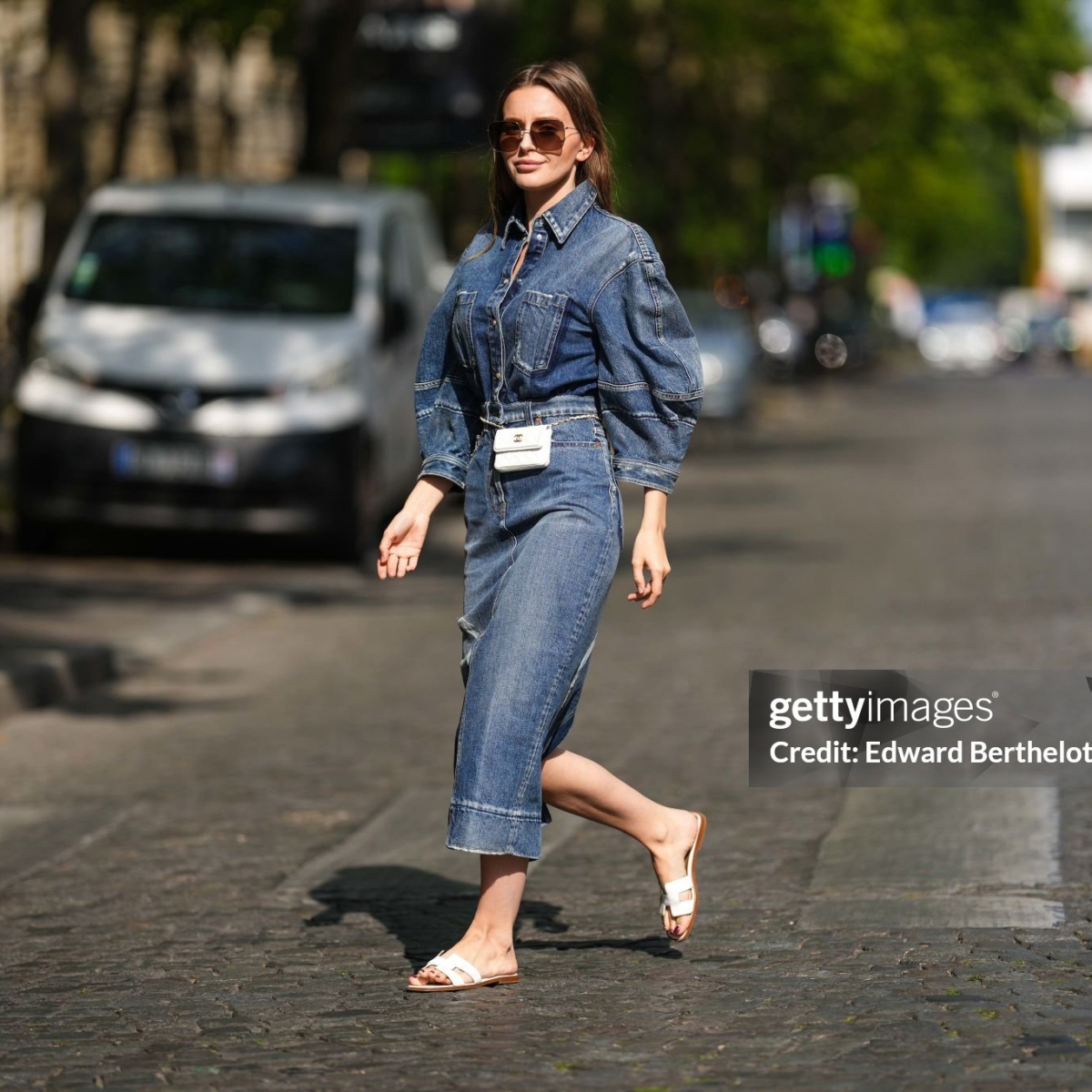 PARIS, FRANCE - APRIL 27: Diane Batoukina wears brown sunglasses from Dior, a blue faded / ripped oversized / puffy shoulders / buttoned and printed pattern long denim dress from Valentino, a white leather belt bag from Chanel, white leather Oran sandals from Hermès, during a street style fashion photo session, on April 27, 2022 in Paris, France. (Photo by Edward Berthelot/Getty Images)