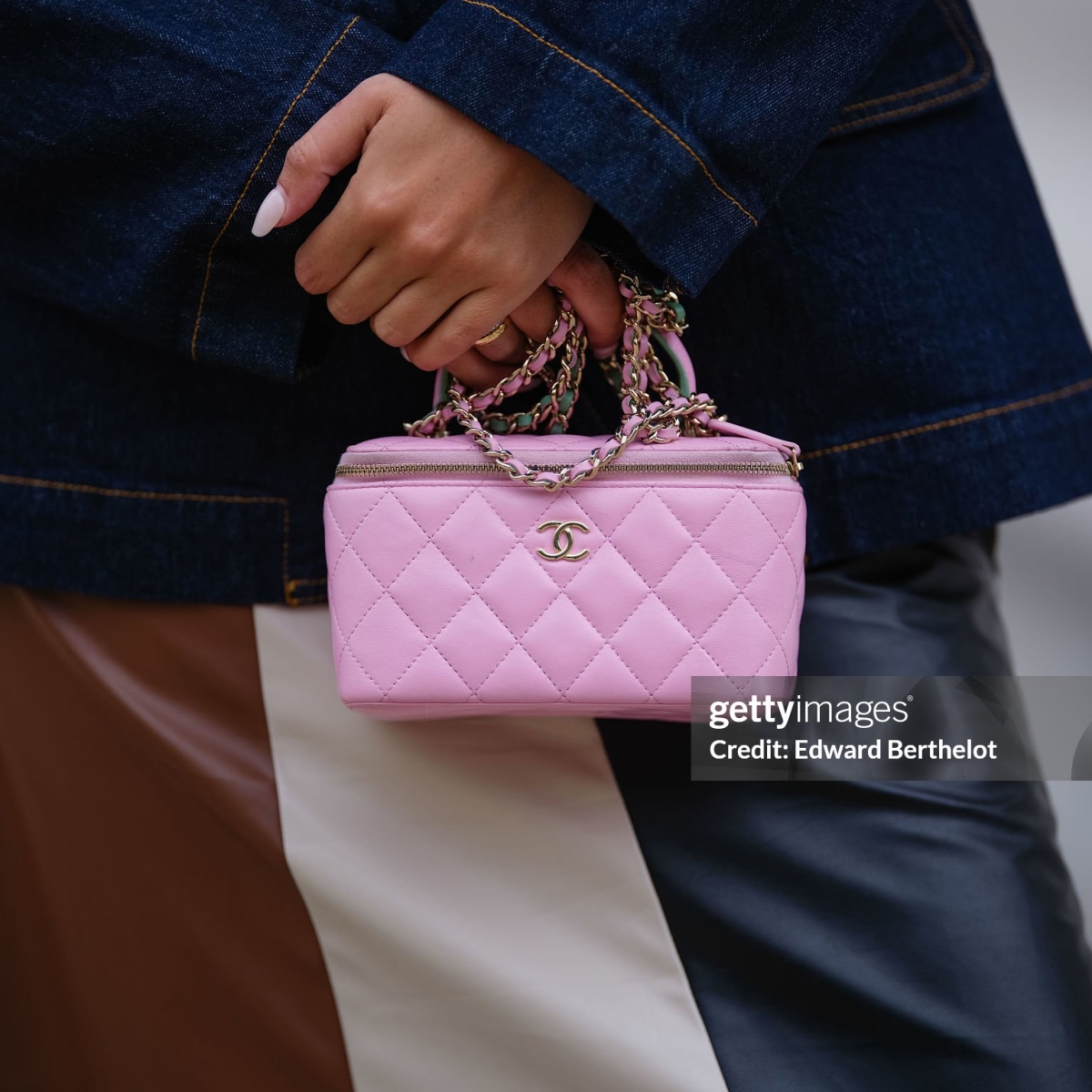 PARIS, FRANCE - APRIL 25: Gabriella Berdugo wears a quilted pink vanity bag by Chanel with a top handle and leather-woven chain strap, styled with a navy denim blazer by Baum und Pferdgarten and a color-block patchwork leather midi skirt, captured in a close-up / detail shot, during a street style fashion photo session, on April 25, 2025 in Paris, France. (Photo by Edward Berthelot/Getty Images)