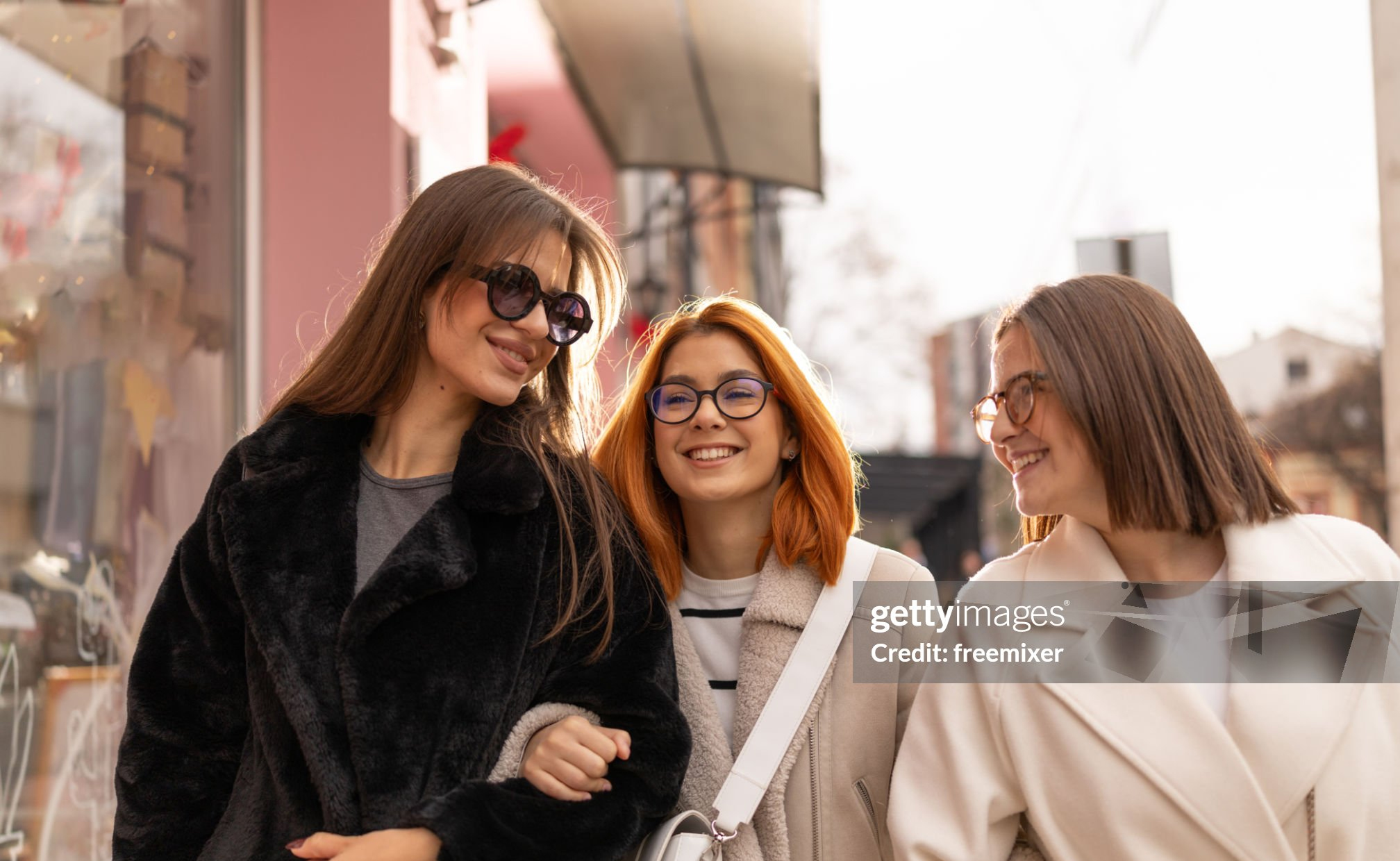 Portrait of three fashionable young female friends walking in the city on sunny winter day Getty Image