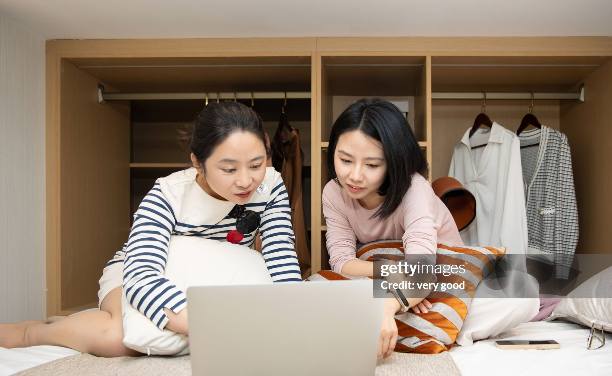 Two happy Asian women sitting on bed and using laptop to surf the internet Getty Image