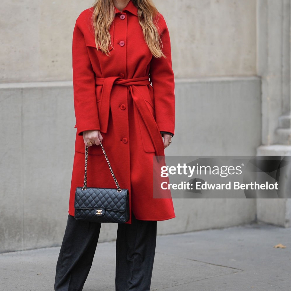 PARIS, FRANCE - DECEMBER 05: Maria Rosaria Rizzo wears long light brown hair worn loose with a center part, natural skin with neutral lipstick, gold hoop earrings, a red wool coat by Elena Miro featuring a button front and a belt, grey wide leg tailored trousers, black pointed toe high heel shoes by Casadei, and a black quilted leather shoulder bag with a chain strap by Chanel, during a street style fashion photo session, on December 05, 2025 in Paris, France. (Photo by Edward Berthelot/Getty Images)